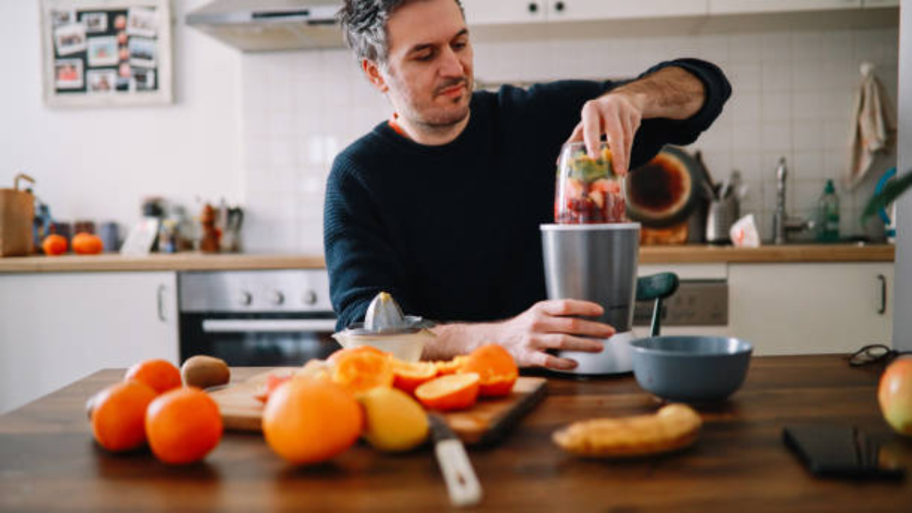 Man preparing a healthy breakfast at home, cutting fruits for a smoothie in his kitchen.